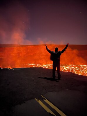 A person standing with arms raised in front of a lava flow.