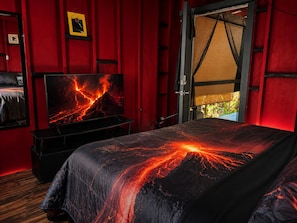 A room with a bed featuring a lava flow design, a television on a stand, and a door leading to an outdoor area.
