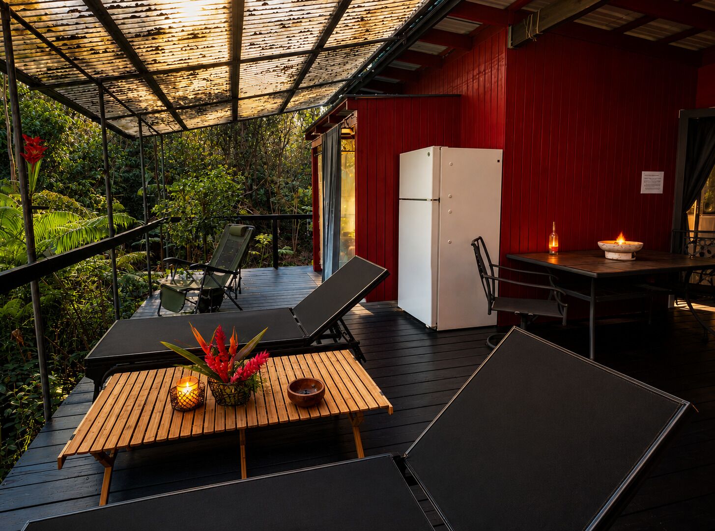A covered outdoor area with a wooden deck, seating, a refrigerator, and a table with a candle.