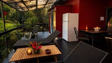 A covered outdoor area with a wooden deck, seating, a refrigerator, and a table with a candle.