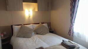A neatly made bed with two pillows, a bedside table with a lamp, and a window with curtains. - Comfy golf course view at Lilliardsedge (Jedburgh)