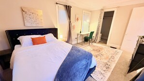 Ein Hotelzimmer mit Bett, Schreibtisch und Stuhl. Es gibt ein Fenster mit Vorhängen, eine Heizung und eine Tür.