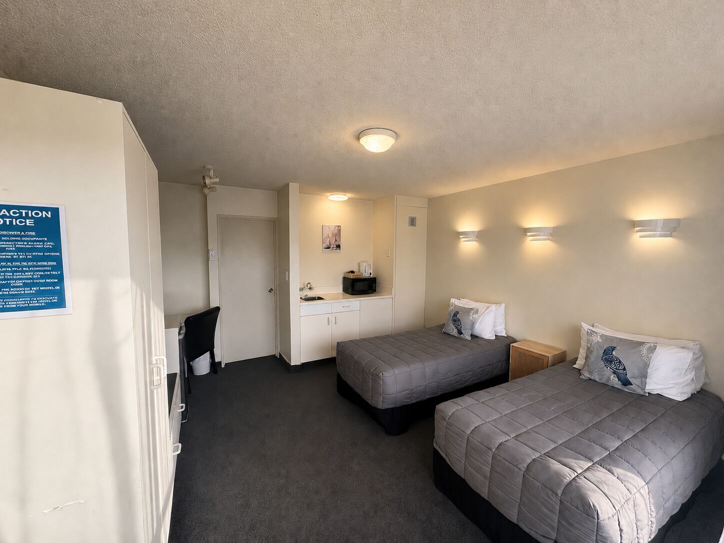 A hotel room with two beds, a kitchenette, a bathroom, and a ceiling light.