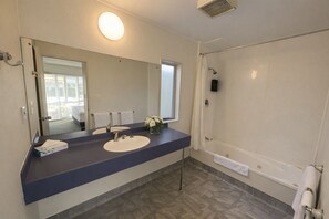 A bathroom with a large mirror, a sink, a shower, and a window. - BK's Fountain Court Motel (Napier)