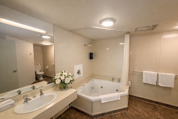 Un baño con lavamanos doble, bañera, ducha, espejo y un jarrón con flores.