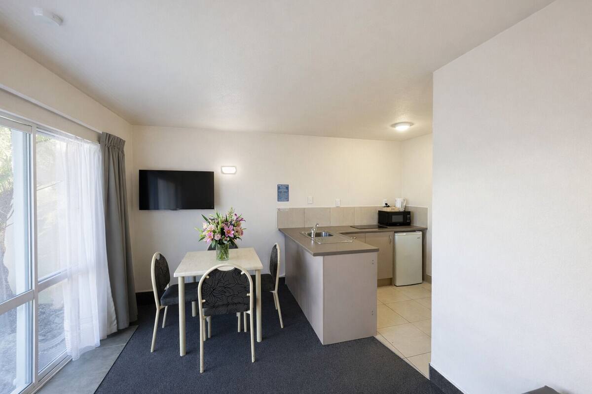 A compact hotel room with a dining area, kitchenette, and a flat-screen TV.