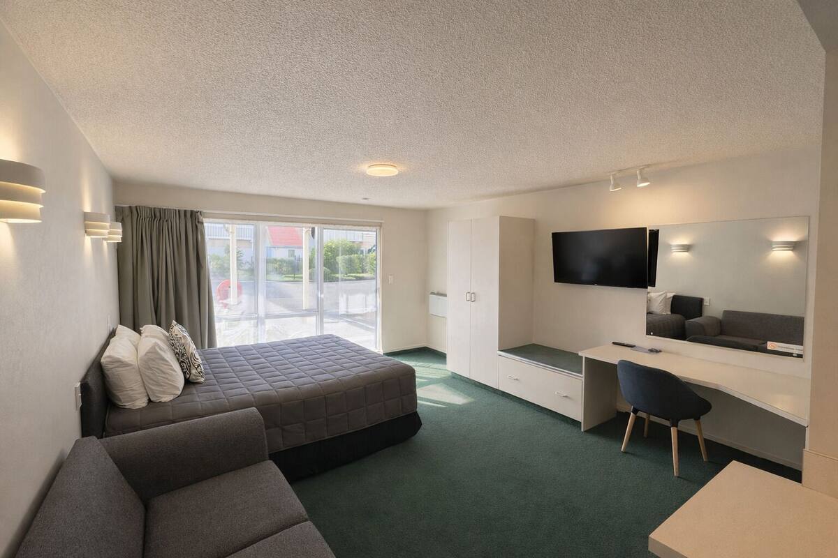 A hotel room with a bed, a desk, a chair, a TV, and a large window.