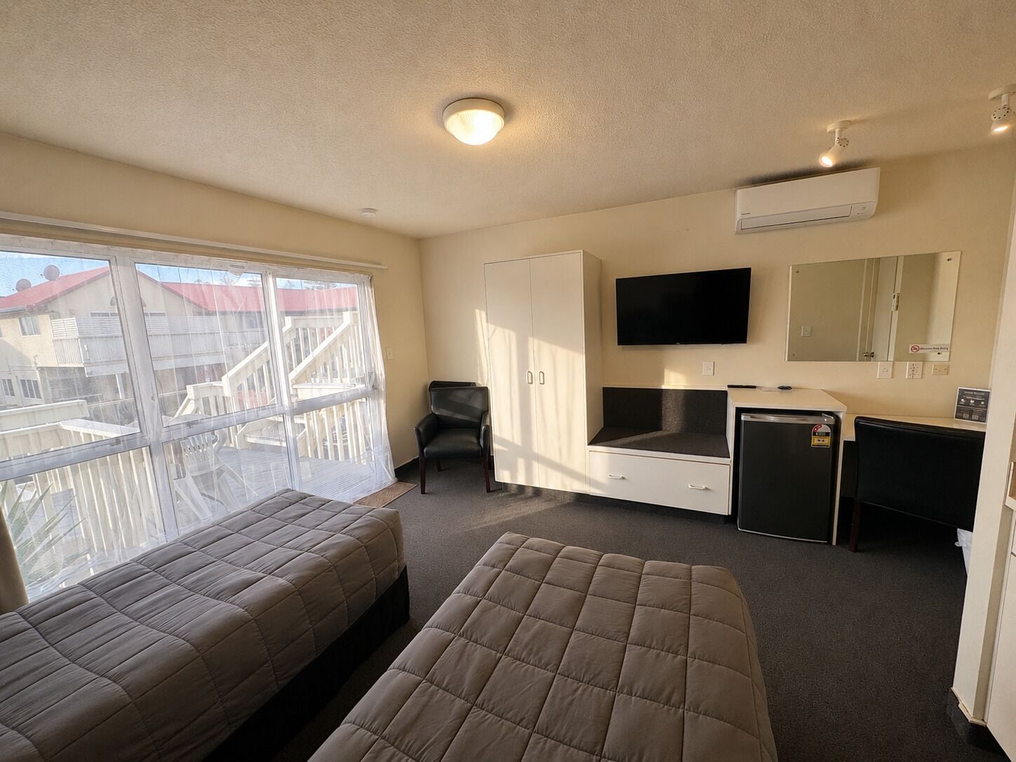 Una habitación con dos camas, un escritorio, una silla, un televisor y aire acondicionado.