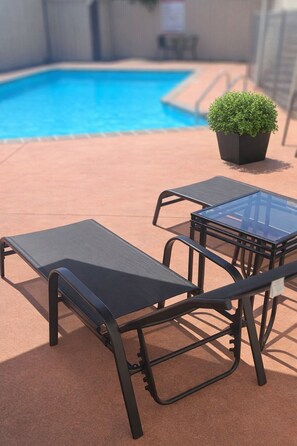 A poolside area with a lounge chair, a table, and a potted plant. - BK's Fountain Court Motel (Napier)