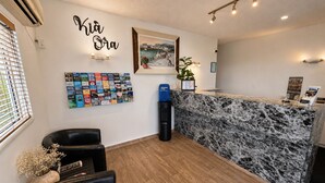 A reception area with a marble counter, a wall-mounted photo, a bulletin board, and a black leather chair. - BK's Fountain Court Motel (Napier)