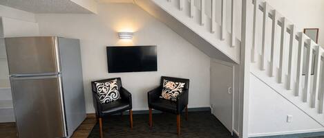 A modern living room with a staircase, a flat-screen TV, and a refrigerator.