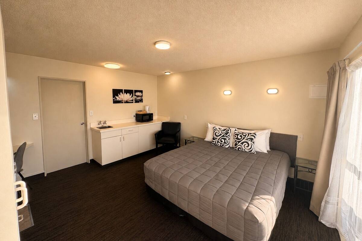 A hotel room with a bed, a desk with a chair, a microwave, and a small cabinet.