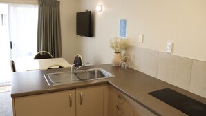 A compact kitchenette with a sink, a flat-screen TV mounted on the wall, and a vase with dried flowers on the counter. - BK's Fountain Court Motel (Napier)