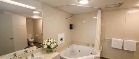 A bathroom with a double sink, a bathtub, a shower, a mirror, and a vase of flowers.