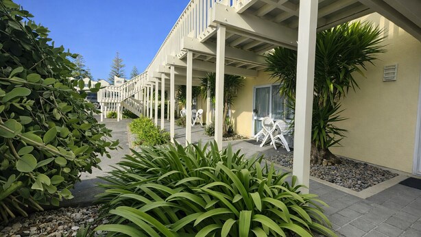 A hotel corridor with a covered walkway, outdoor seating, and greenery. - BK's Fountain Court Motel (Napier)