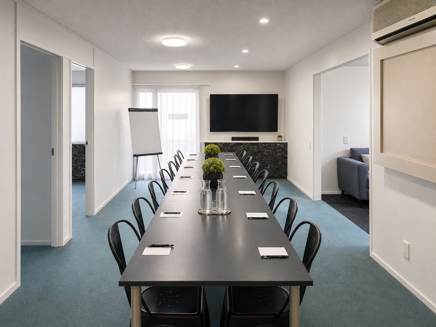 Ein Konferenzraum mit einem langen Tisch, Stühlen, einer Whiteboard-Tafel und einem Flachbildfernseher.