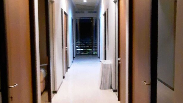 A hotel corridor with wooden doors, a tiled floor, and a view of a cityscape through the windows. - Phoenix Living (Surabaya)