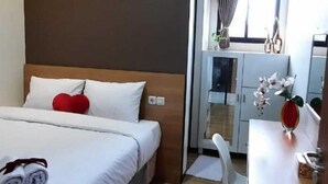 A hotel room with a bed, a desk, an air conditioning unit, and a view of the bathroom. - Phoenix Living (Surabaya)