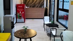A modern reception area with a marble wall, a Coca-Cola refrigerator, and seating arrangements. - Phoenix Living (Surabaya)