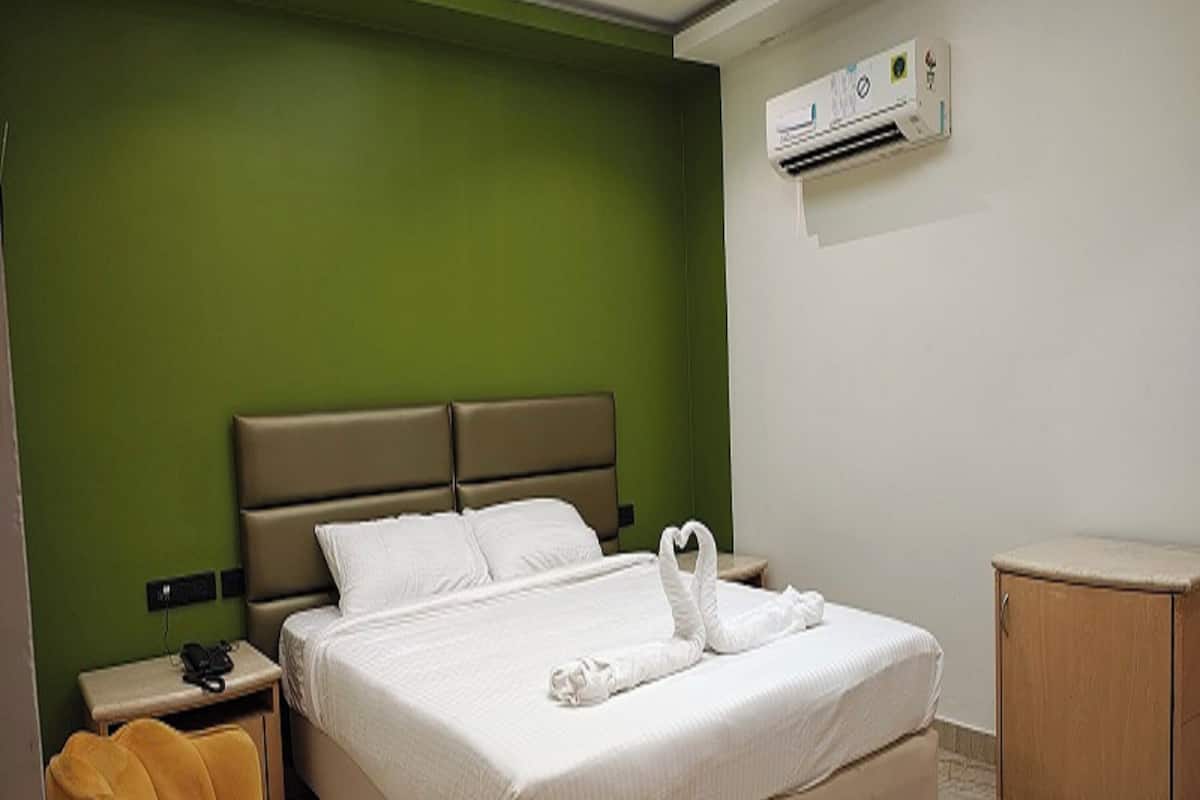A hotel room with a bed, a nightstand, a chair, an air conditioning unit, and a wooden cabinet.