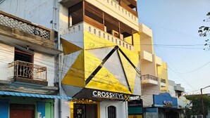 A building with a prominent yellow and black geometric design on the facade, a visible storefront with the name "Crosskeys" and a sign for "The Hotel", and a street scene with a cyclist. - The Cloud Hotel (Puducherry)