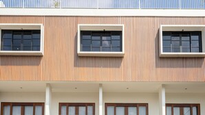 A modern building with three balconies, each with a glass railing and wooden furniture.