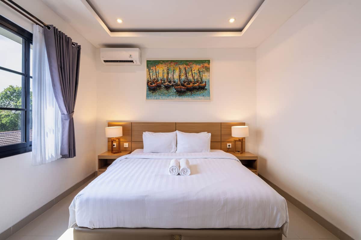 Habitación de hotel con una cama grande, dos lámparas de noche, un cuadro en la pared y una ventana con cortinas.