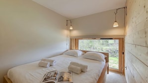 A bedroom with a large bed, two bedside lamps, a window with a view, and a magazine on the bed.