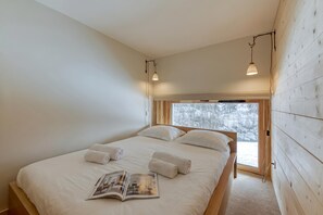A bedroom with a large bed, two bedside lamps, a window with a view of trees, and a magazine on the bed.