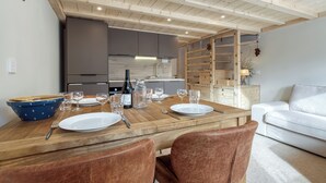 A dining area with a wooden table set for four, a kitchen in the background, and a white sofa.