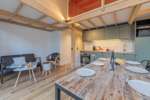Una cocina moderna con vigas de madera, una mesa de comedor para cuatro personas y un sofá gris en la sala de estar.