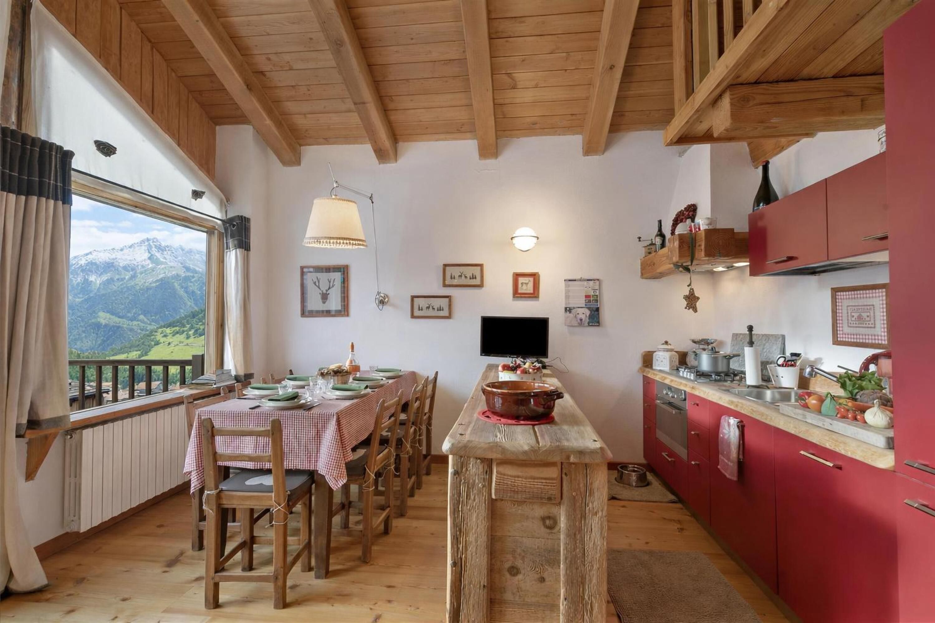 Una cucina rustica con travi in legno, un tavolo da pranzo per quattro persone e vista sulle montagne attraverso una finestra.