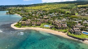 Luftaufnahme eines Küstenresorts mit mehreren bungalowsartigen Gebäuden, einem zentralen Pool und einem Strand.