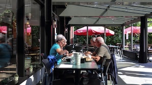 An outdoor cafe with tables and chairs, red umbrellas, and potted plants. - Nature Stay With Garden (Turnhout)