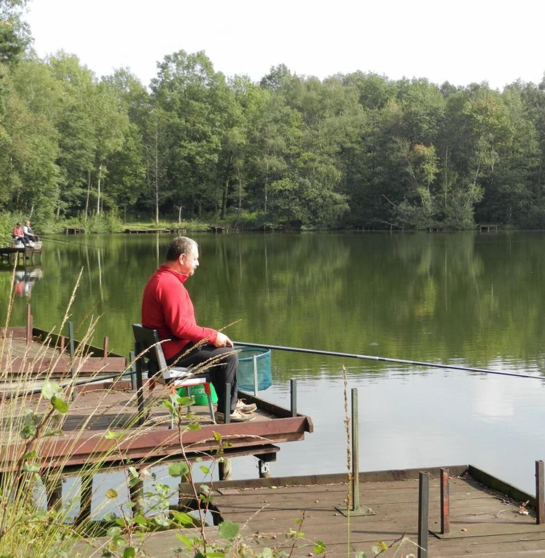 A man sitting on a dock by a calm lake with trees in the background.