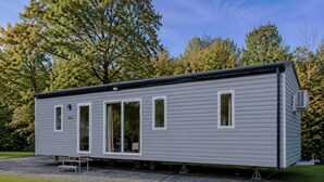 A single-story mobile home with a sliding door, a small porch, and a gravel driveway. - Nature Stay With Garden (Turnhout)