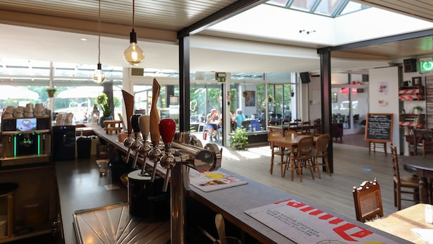 A modern bar area with a long counter, multiple taps, and a menu. - Nature Stay With Garden (Turnhout)