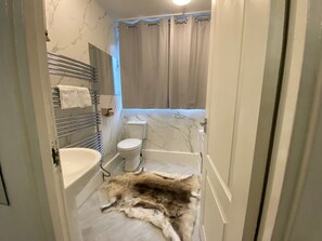 A bathroom with a marble wall, a toilet, a bathtub, and a fur rug on the floor. - London Charm - 3 Bedroom House Near Canary Wharf (London)