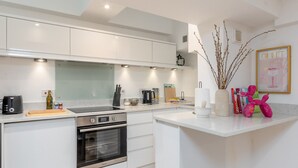 A modern kitchen with white cabinetry, a built-in oven, and a countertop with various appliances and utensils. - Clarendon Place - Stunning 1BD in Leamington Spa (Royal Leamington Spa)