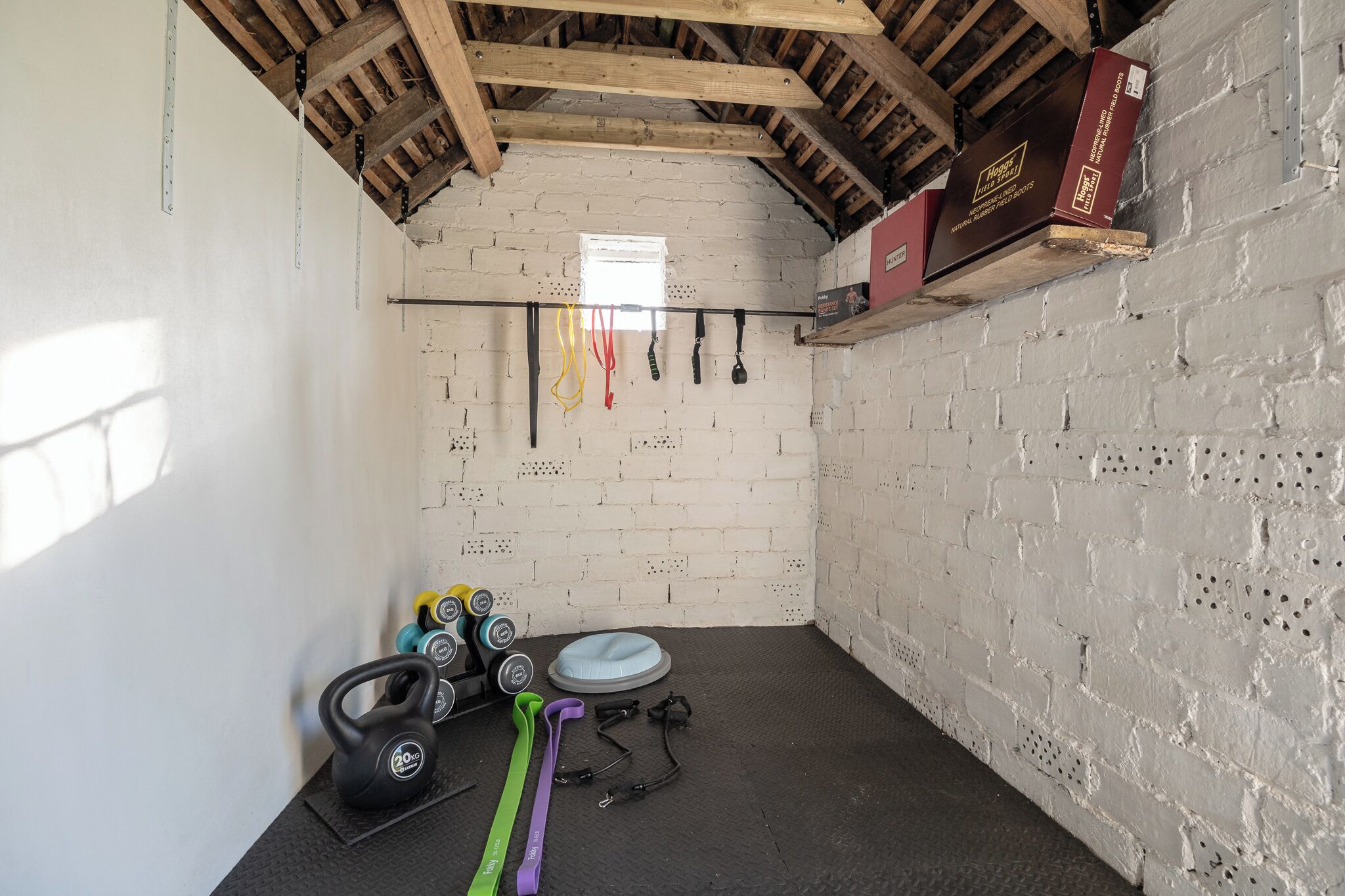 Una palestra con parete in mattoni, travi in legno e attrezzature per esercizi come kettlebell, fasce elastiche e rullo in schiuma.