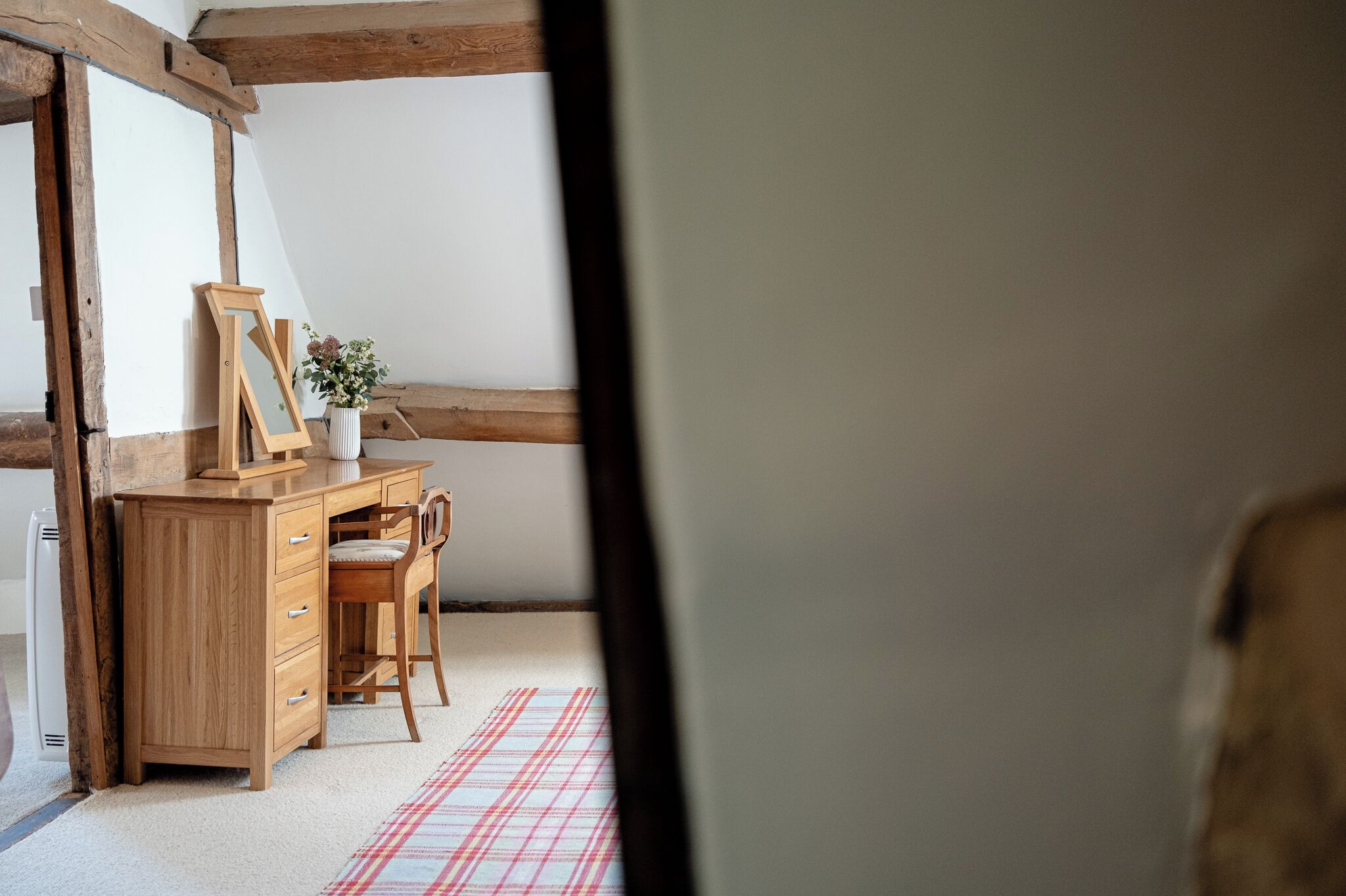 A room with a wooden desk, a chair, a framed picture, and a vase with flowers.
