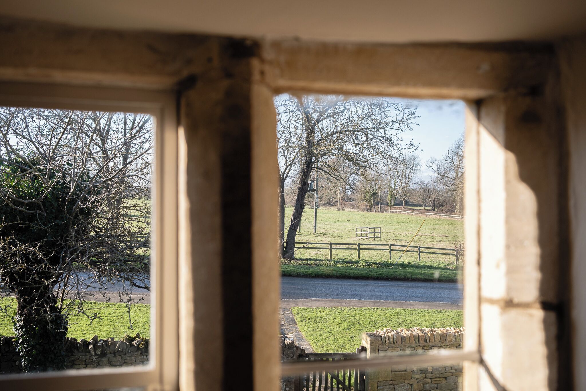 Vista a través de una ventana que muestra un paisaje rural con un muro de piedra, un campo cubierto de hierba y una valla de madera.
