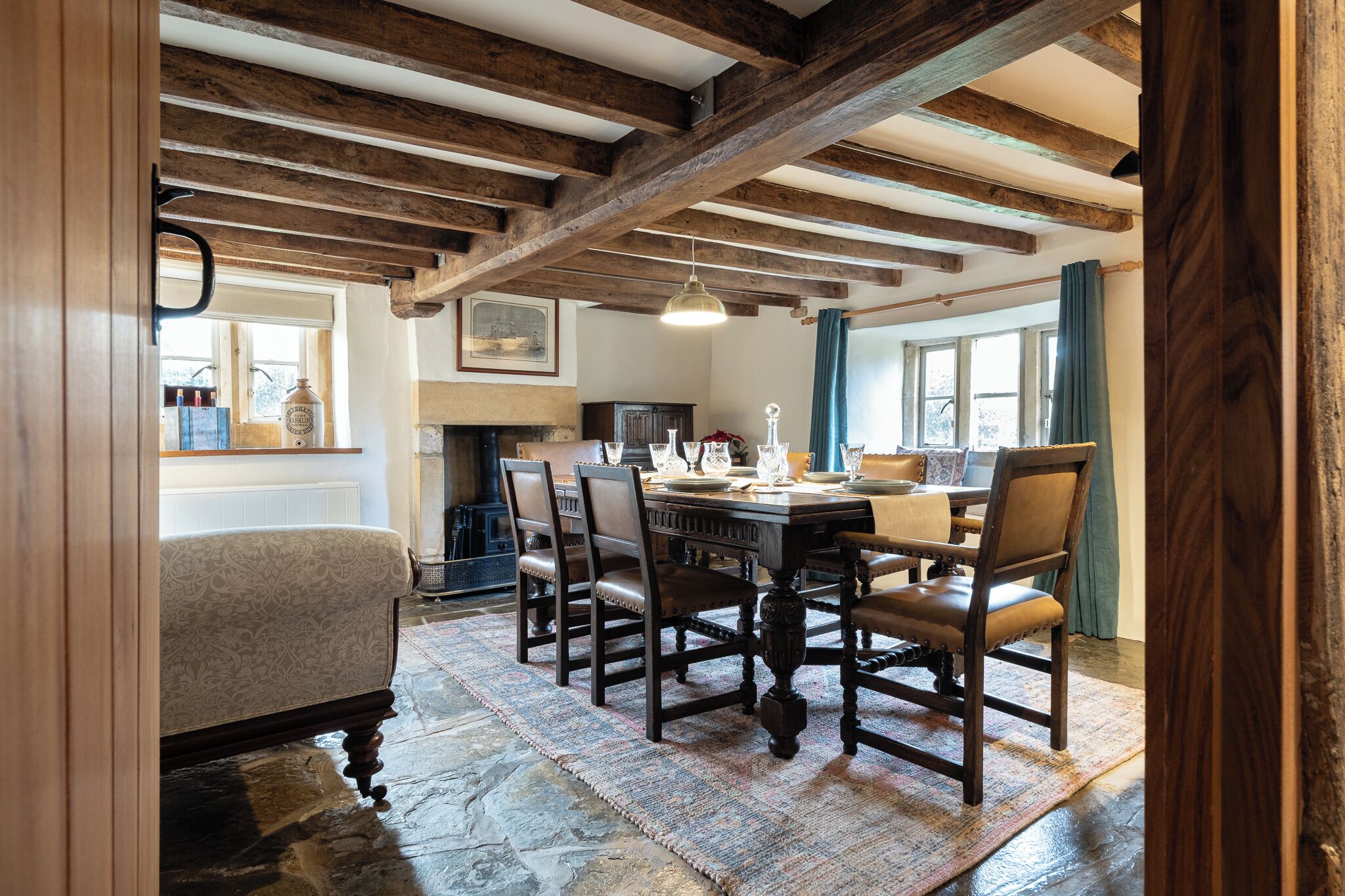 A dining area with a wooden table and chairs, a patterned sofa, and a stone floor.