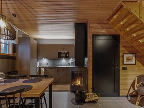 Una cocina acogedora con estufa de leña, comedor con mesa y sillas, y encimera de cocina con electrodomésticos.