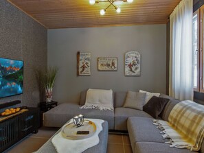 A living room with a sofa, a coffee table, a TV, and wall art depicting skiing scenes.