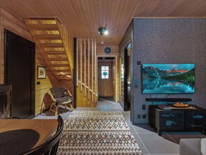 Un interior de madera con una escalera, un televisor montado en una pared con textura y un área de comedor con alfombra estampada.