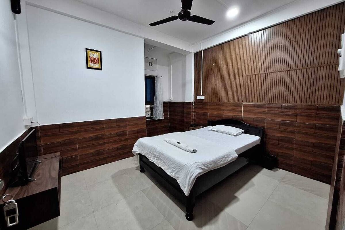 Ein Schlafzimmer mit Bett, Deckenventilator, Wandverkleidung aus Holz und einem kleinen Schreibtisch mit Stuhl.
