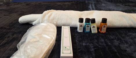 A neatly arranged set of toiletries on a bed with a dark blue cover, including a white towel, a box, and several bottles of personal care products.