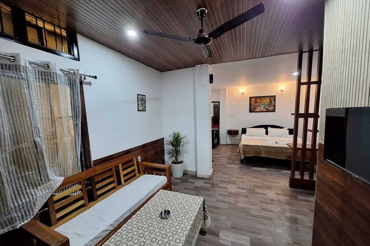 Ein Zimmer mit Holzboden, Deckenventilator, Bett, Tisch und Fernseher.