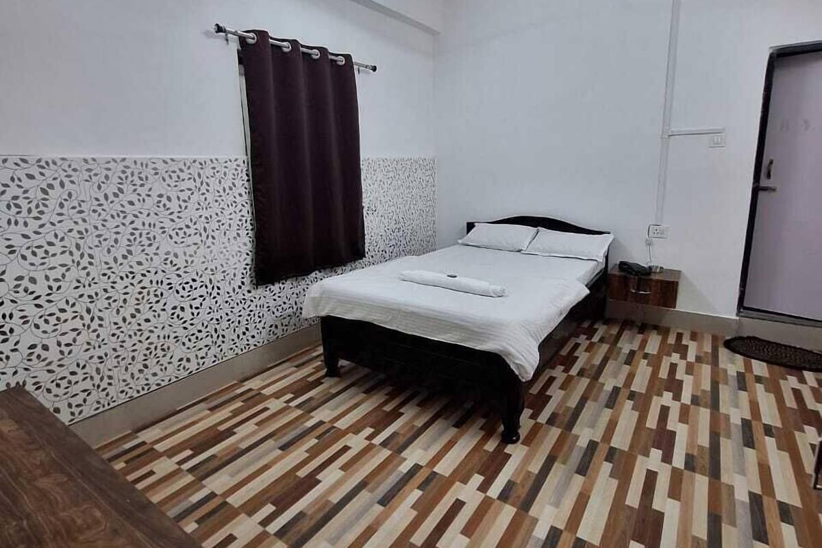 Ein Schlafzimmer mit Bett, Deckenventilator, Fenster mit Vorhängen und einem gemusterten Boden.